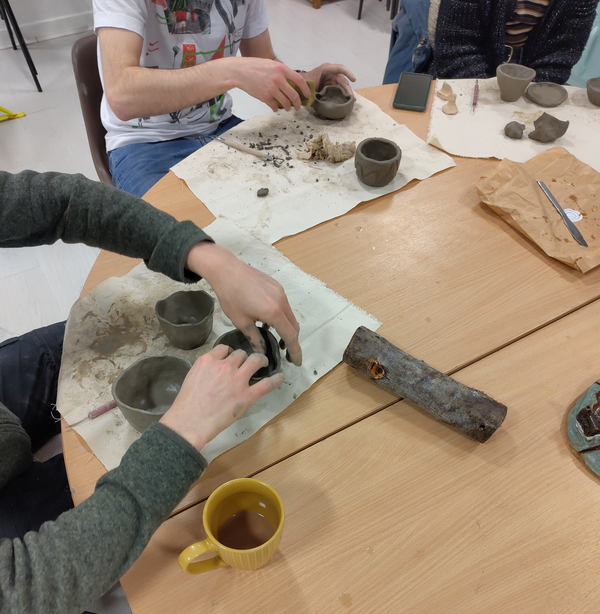 People sitting around a table making pots out of clay at a ceramics workshop. 
